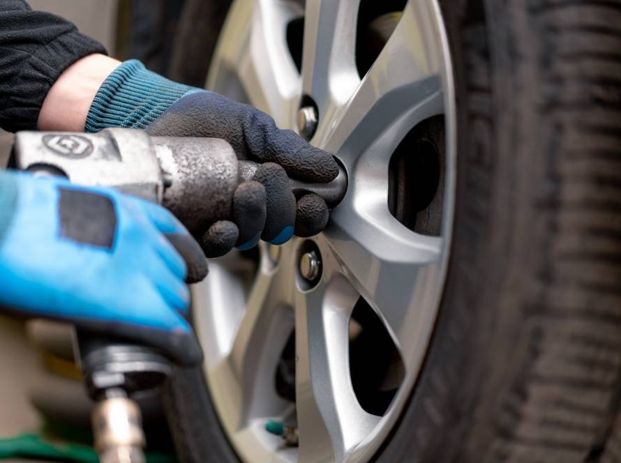Auto mechanic changing a wheel from a black car using a drill in a tire shop
